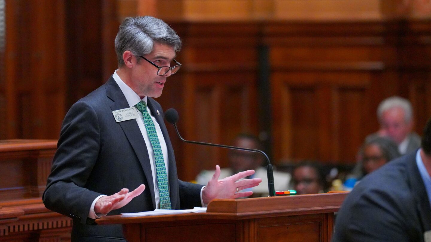 georgia lawmaker shaw blackmon is in a suit and blue tie as he stands in the well of the georgia house of representatives