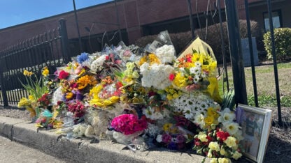 A large pile of flowers on the side of a road outside a school