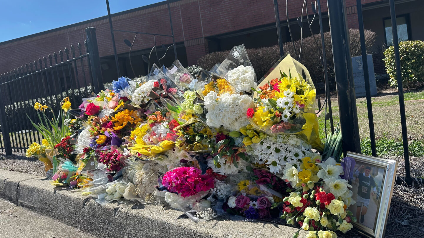 Numerous colorful flower bouquets lined along a fence at North Hall High School.