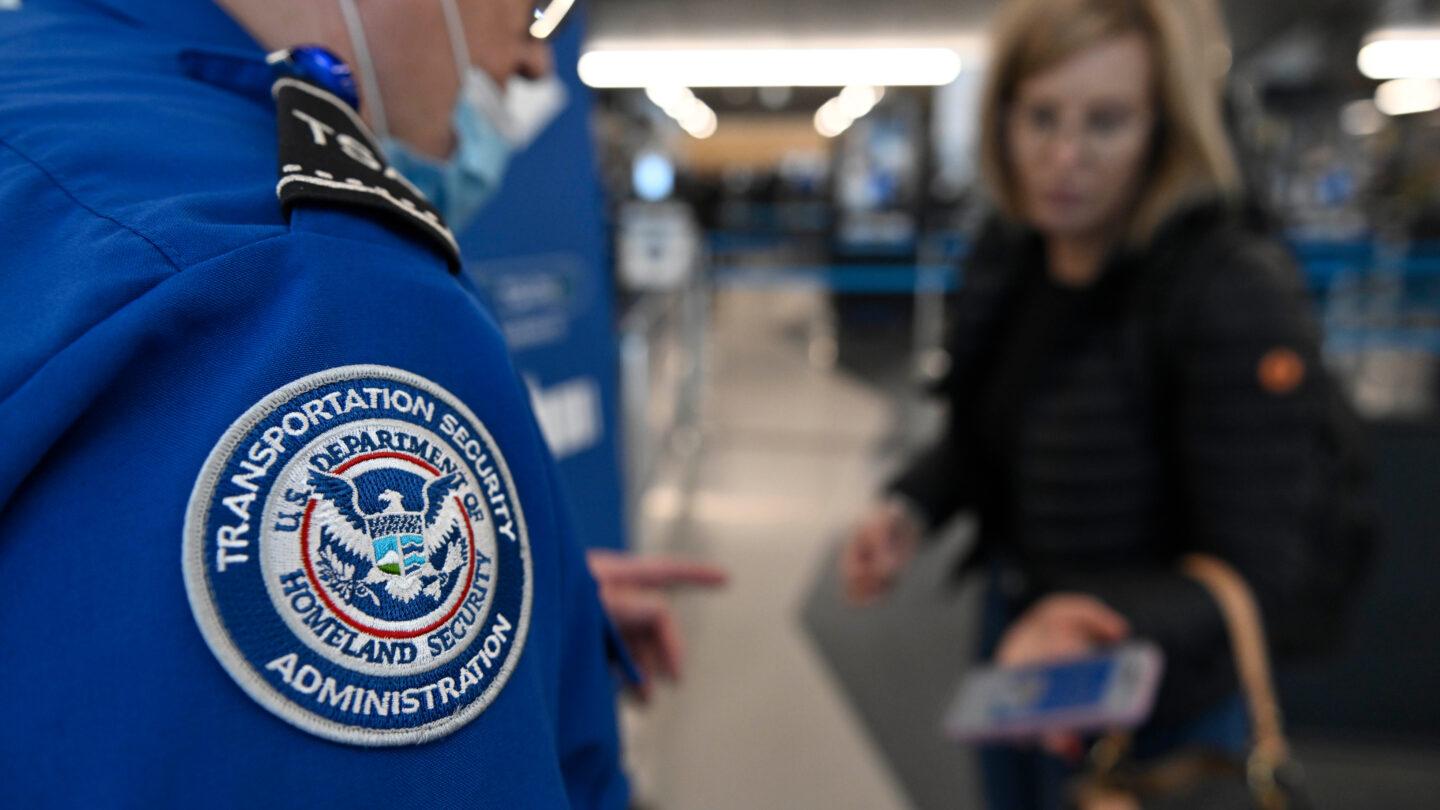 A TSA agent with a badge on his blue uniform checks a passengers ticket