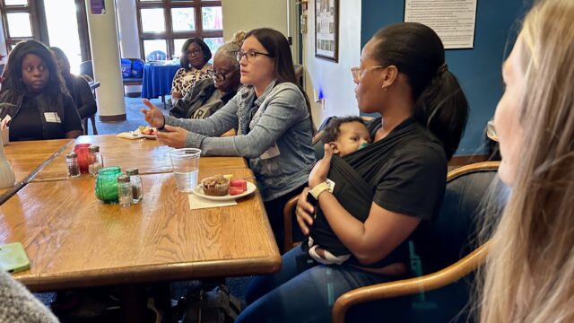 women with babies sit around a wooden table.