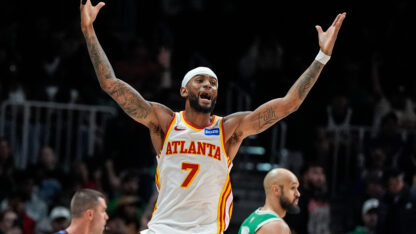 A man wearing a white Atlanta basketball jersey raises his arms up in celebration