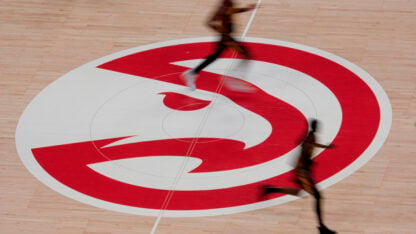 Players run over the red and white Hawks logo on a basketball court