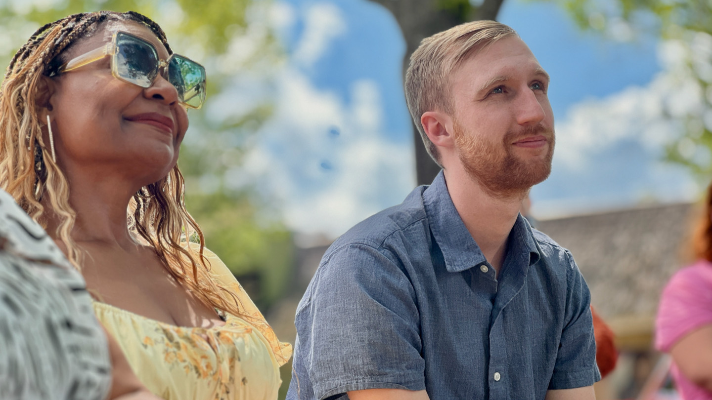 A woman wearing sunglasses sits next to a man wearing a blue shirt