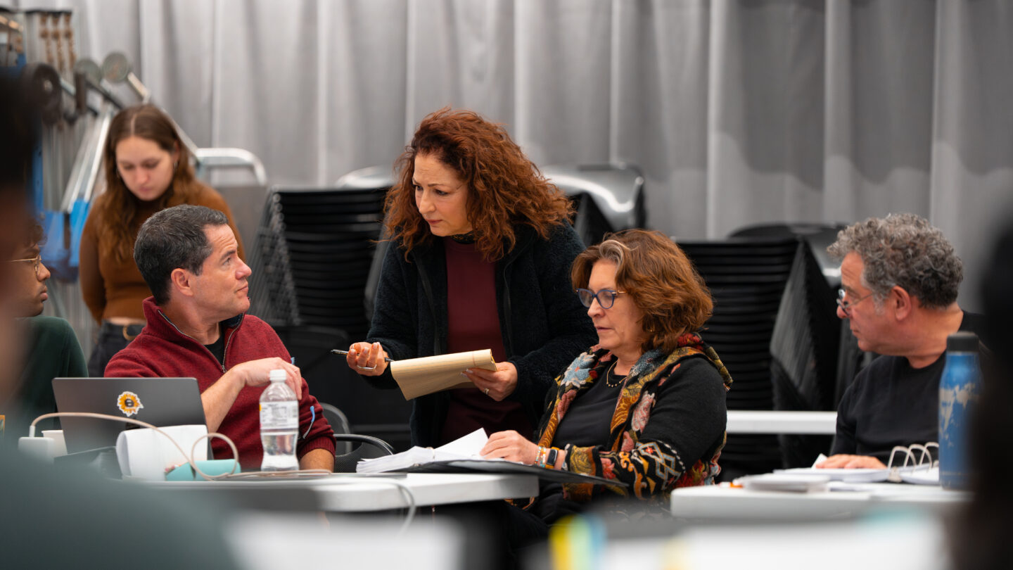 Gloria Estefan stands and confers with seated creative team members during a Basura workshop rehearsal at Alliance Theatre.