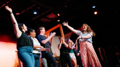 Cast of Road Trip 2 takes a celebratory bow on stage at the 2026 Atlanta Fringe Festival, arms raised and clapping under stage lighting.