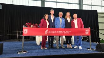 Five people stand in a line behind a red ribbon