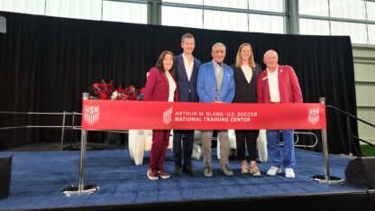 Five people stand in a line behind a red ribbon