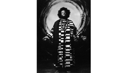 Kamasi Washington stands in bold black-and-white striped robes against a circular backdrop.