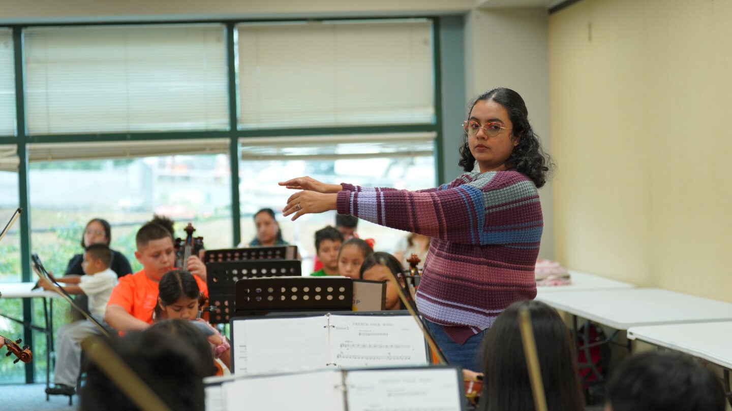A side view of a conductor leading a youth orchestra