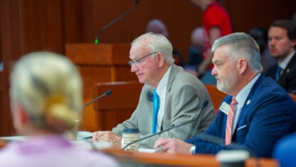 Two men sit at a table at a hearing
