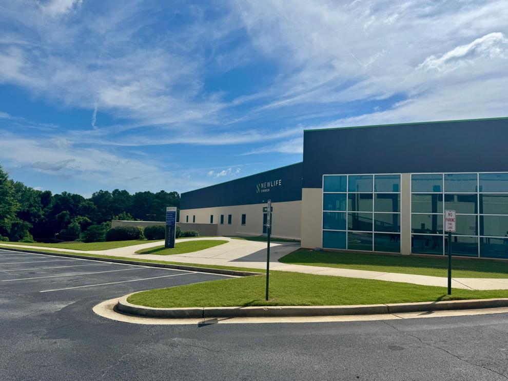 A grey blue and white building with large glass windows behind a parking lot