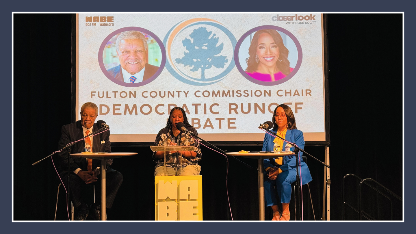 A man, a woman, and another woman wearing a blue pantsuit sit in front of a projected screen with the words Fulton County Commission Chair Democratic runoff debate.