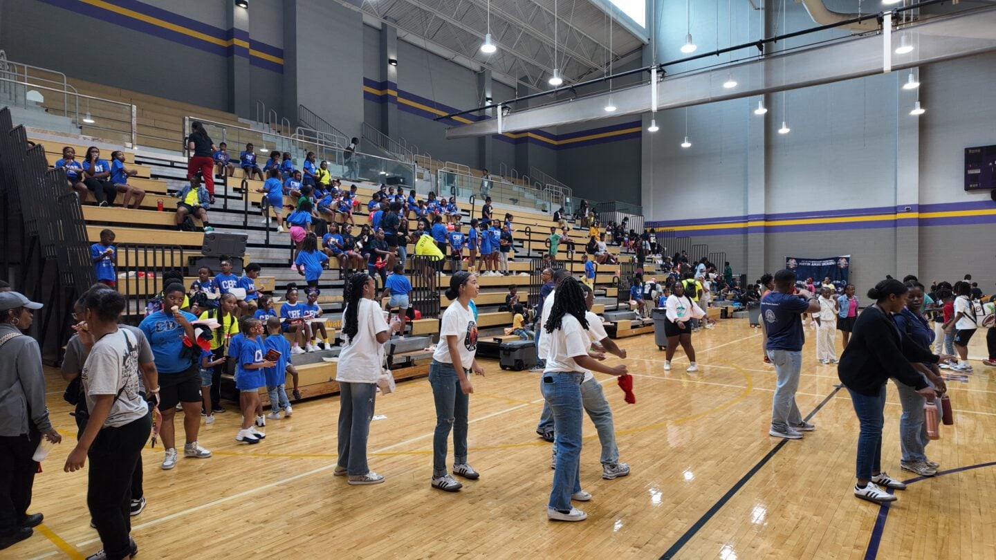 Students standing and sitting in an open gym.
