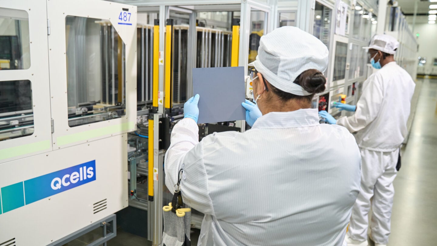 Two workers wearing white apparel and PPE work at a solar cell factory