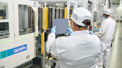 Two workers wearing white apparel and PPE work at a solar cell factory
