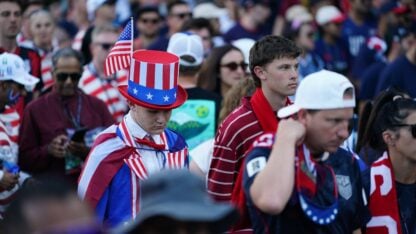 A large group of United States fans wearing USA themed clothing look downtrodden