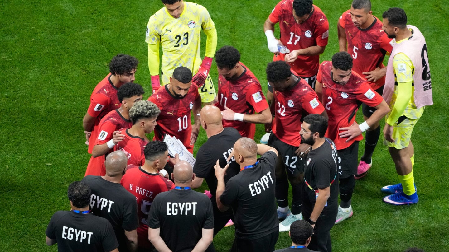 A crowd of soccer players in red jerseys talk to their coach