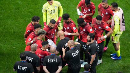 A crowd of soccer players in red jerseys talk to their coach