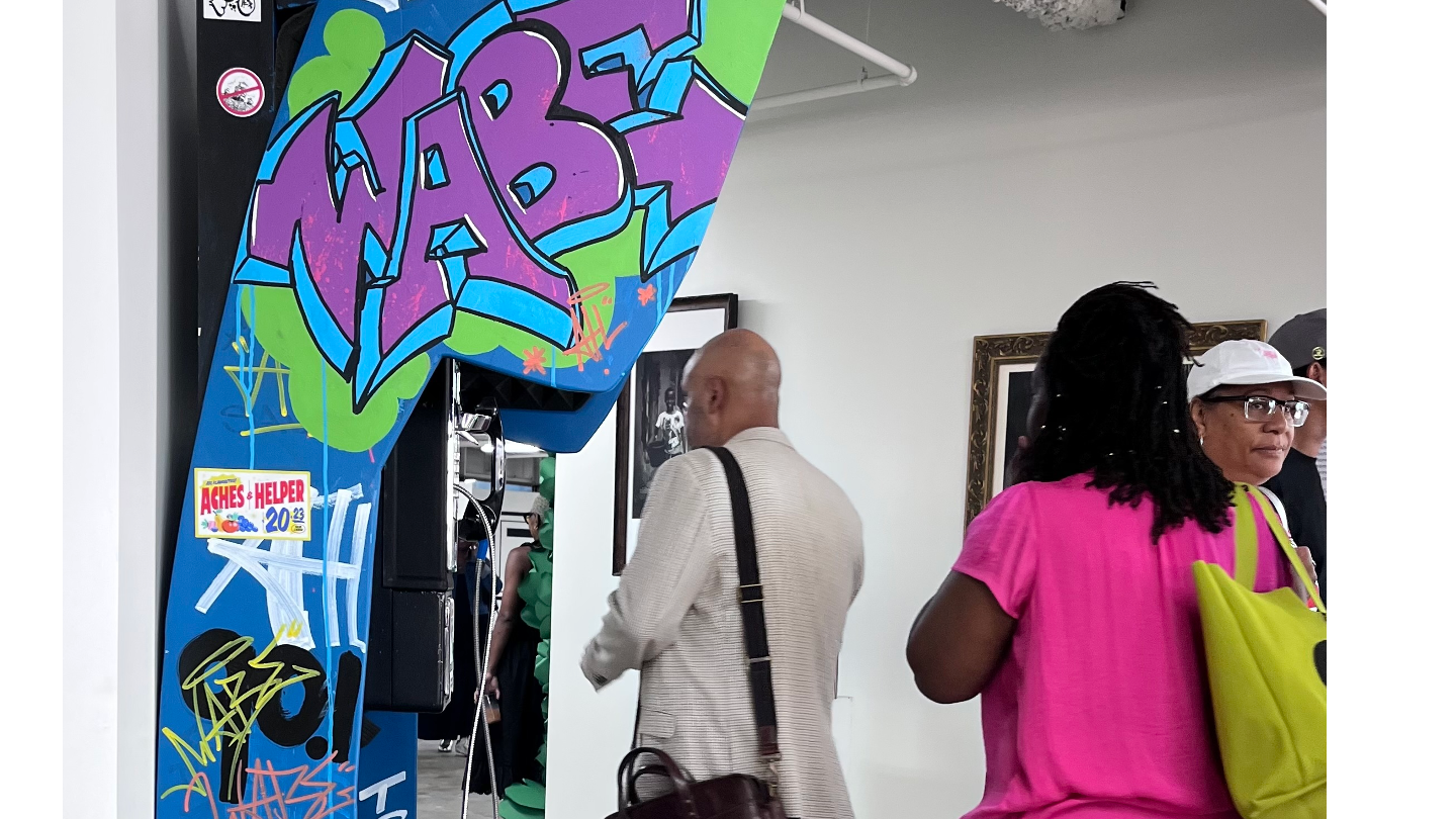 Graffiti-covered blue phone booth activation with a vintage payphone, prompt cards, and an Instagram tag sign, inside the Atlanta Cultural Exchange.