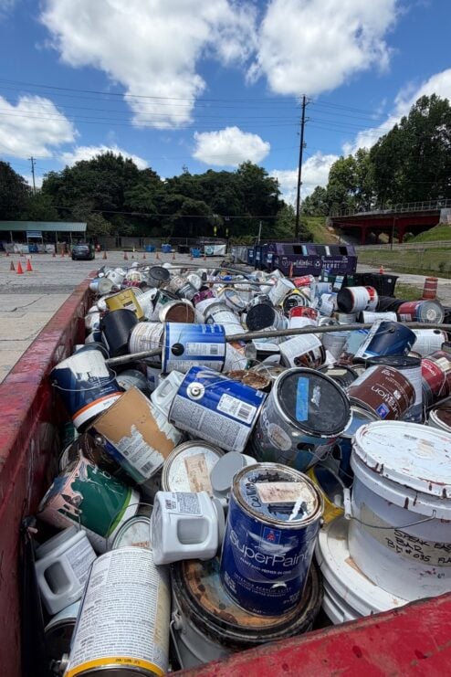 Used paint cans fill a large container.